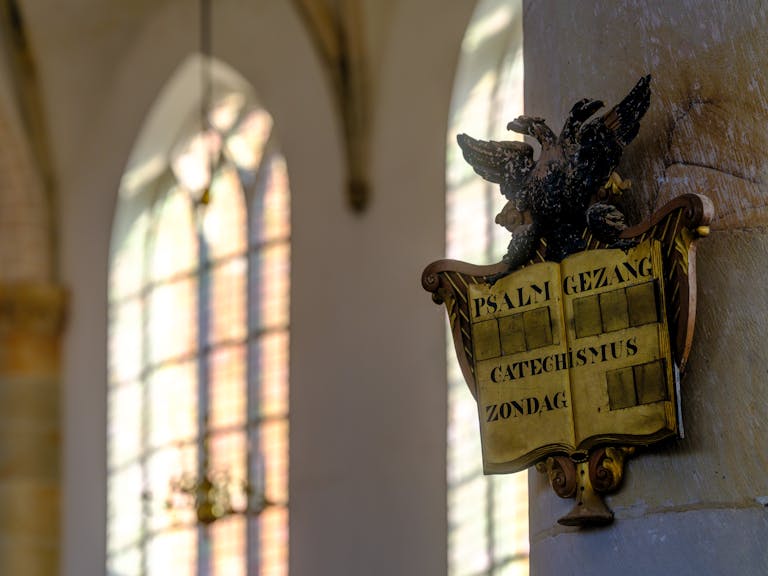 Gothic church interior in Naarden, featuring sunlight filtering through stained glass windows and a psalm board.